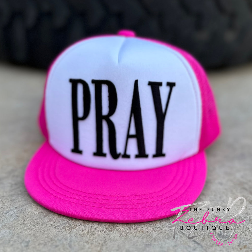 White front face foam trucker hat with hot pink mesh and flat brim bill. The front features PRAY in tall black embroidered letters.