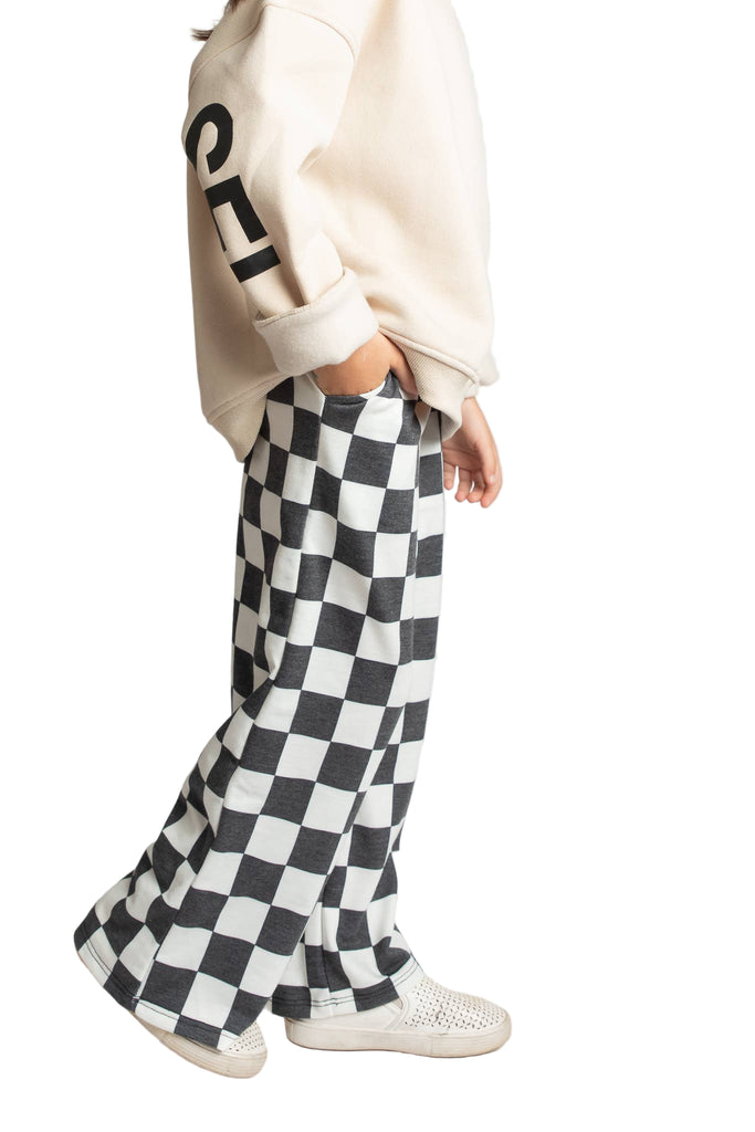 Person wearing a beige sweatshirt and checkered pants on a plain background
