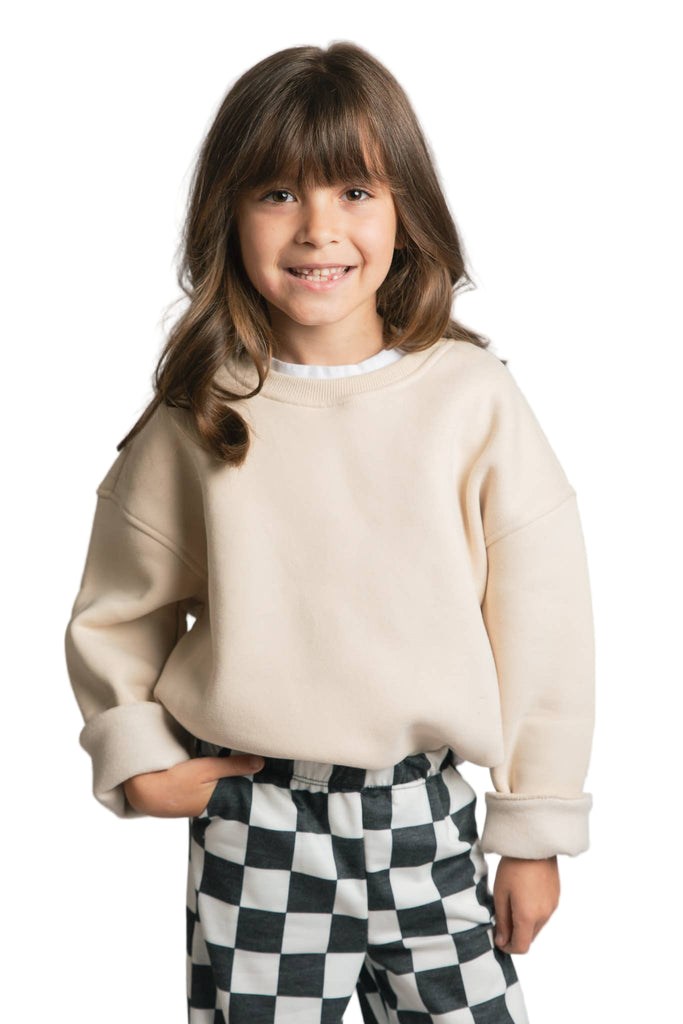Young girl wearing a beige sweater and checkered pants on a plain background