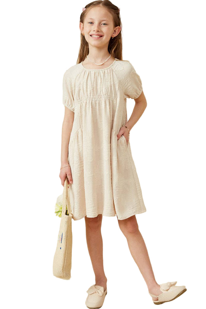 Young girl wearing a white dress holding a yellow flower against a beige background