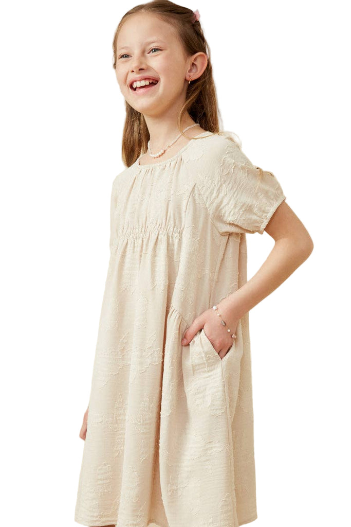 Young girl wearing a beige dress against a plain background