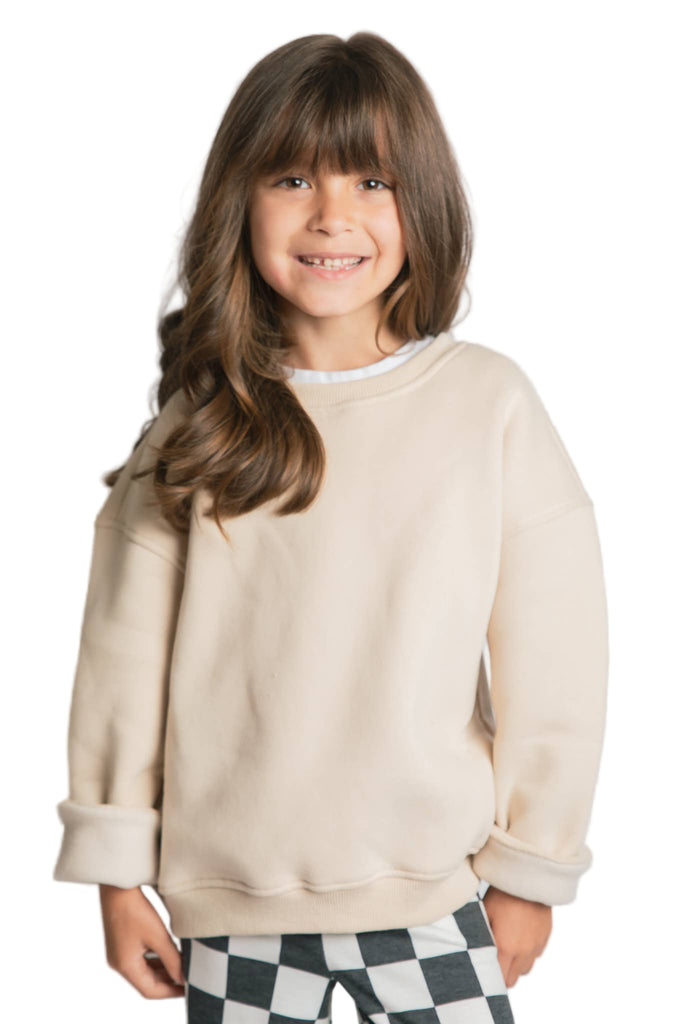 Young girl wearing a beige sweater and checkered pants on a plain background
