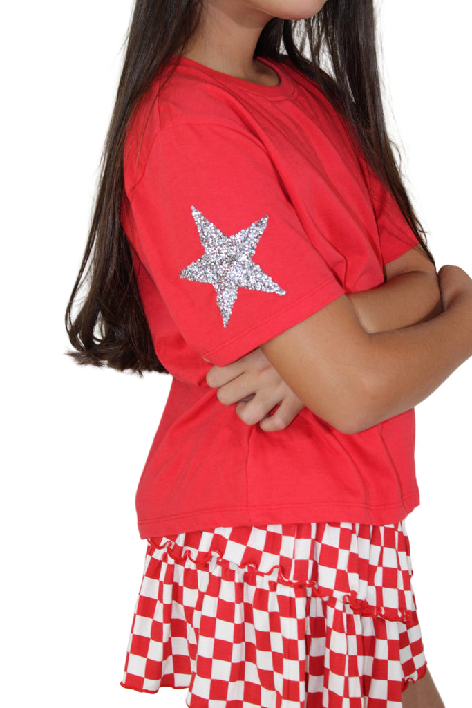 Child wearing a red shirt with a star design and a red and white checkered skirt on a plain background
