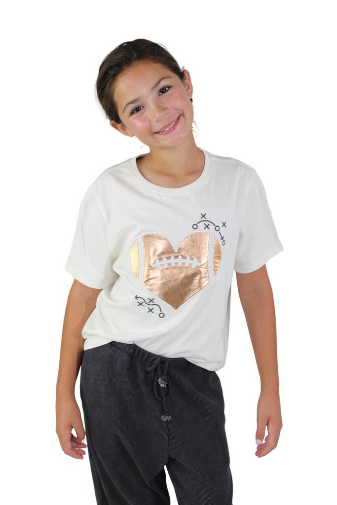 Young girl wearing a white t-shirt with a gold design on a plain background