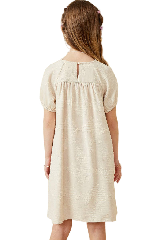 Young girl wearing a beige dress against a plain background
