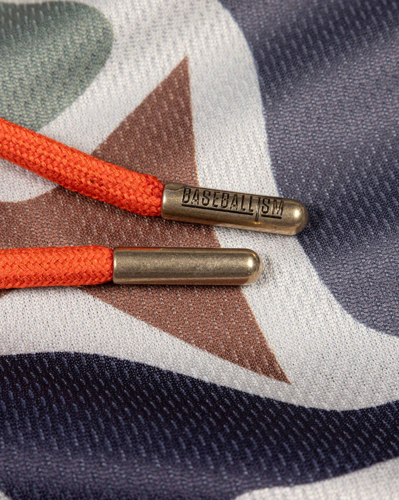 Close-up of orange shoelaces with brass tips on a camouflage-patterned fabric background.