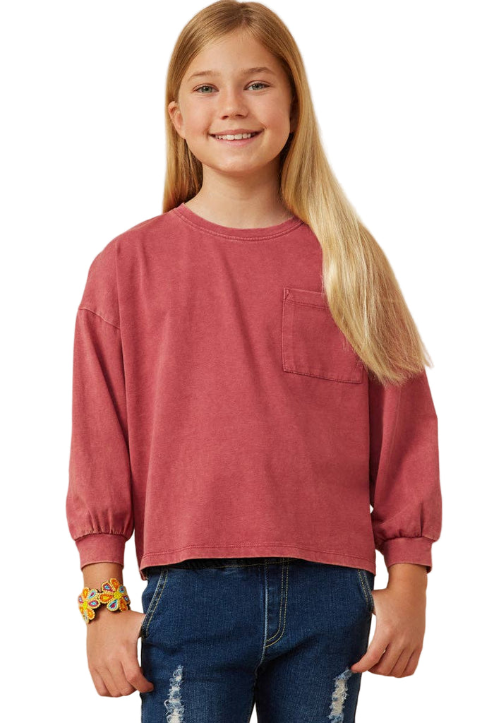 Young girl wearing a red long-sleeve shirt and blue jeans on a beige background