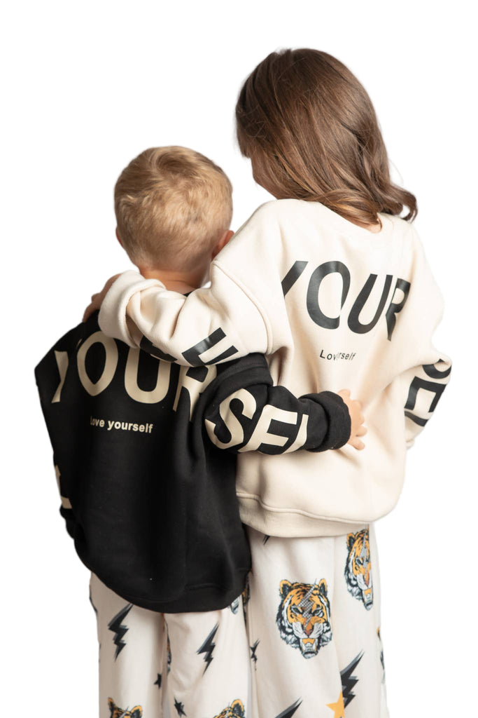 Two children wearing matching hoodies with text on a plain background